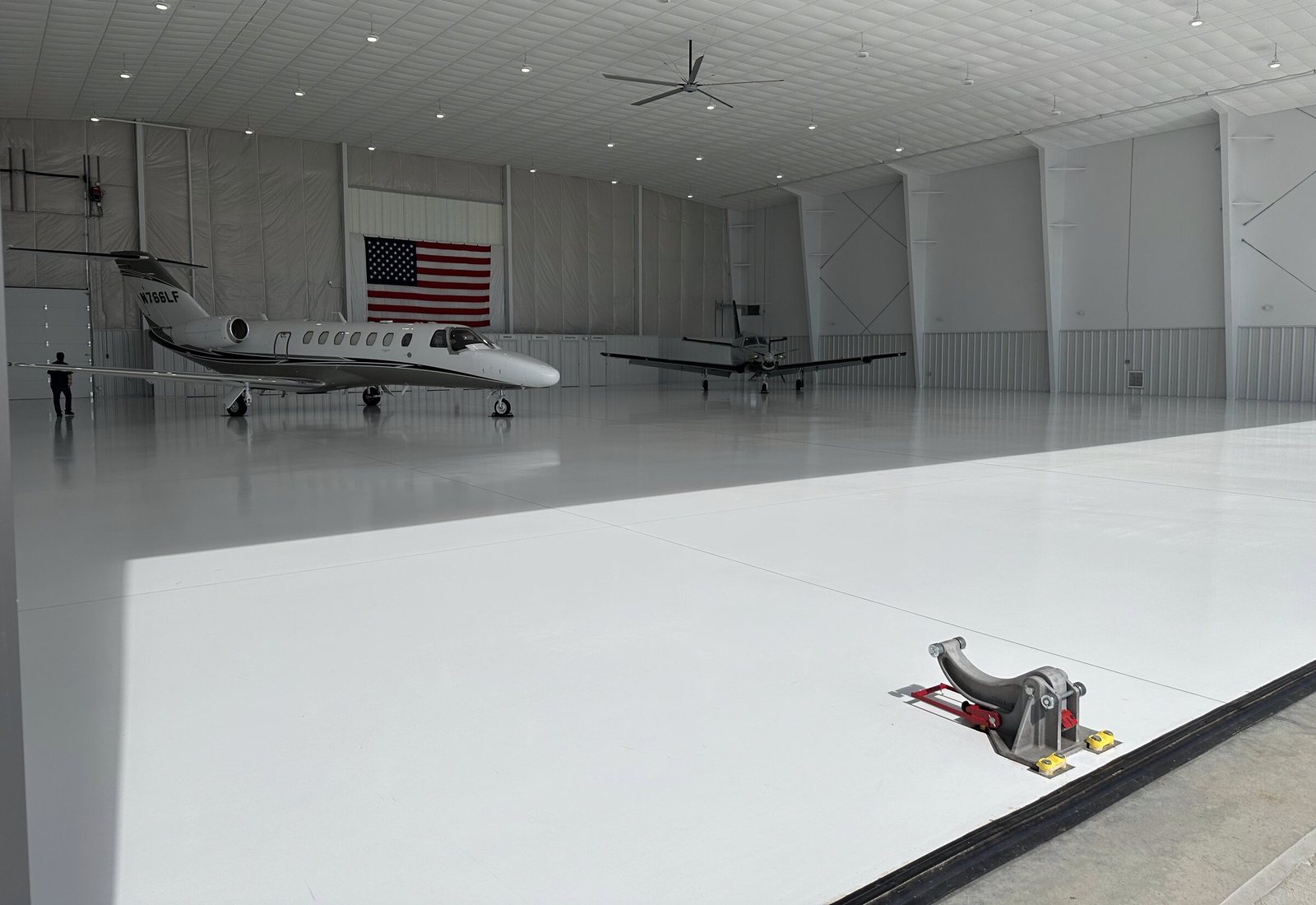 An aircraft tug on the white hangar floor with a jet and a turboprop parked beyond it