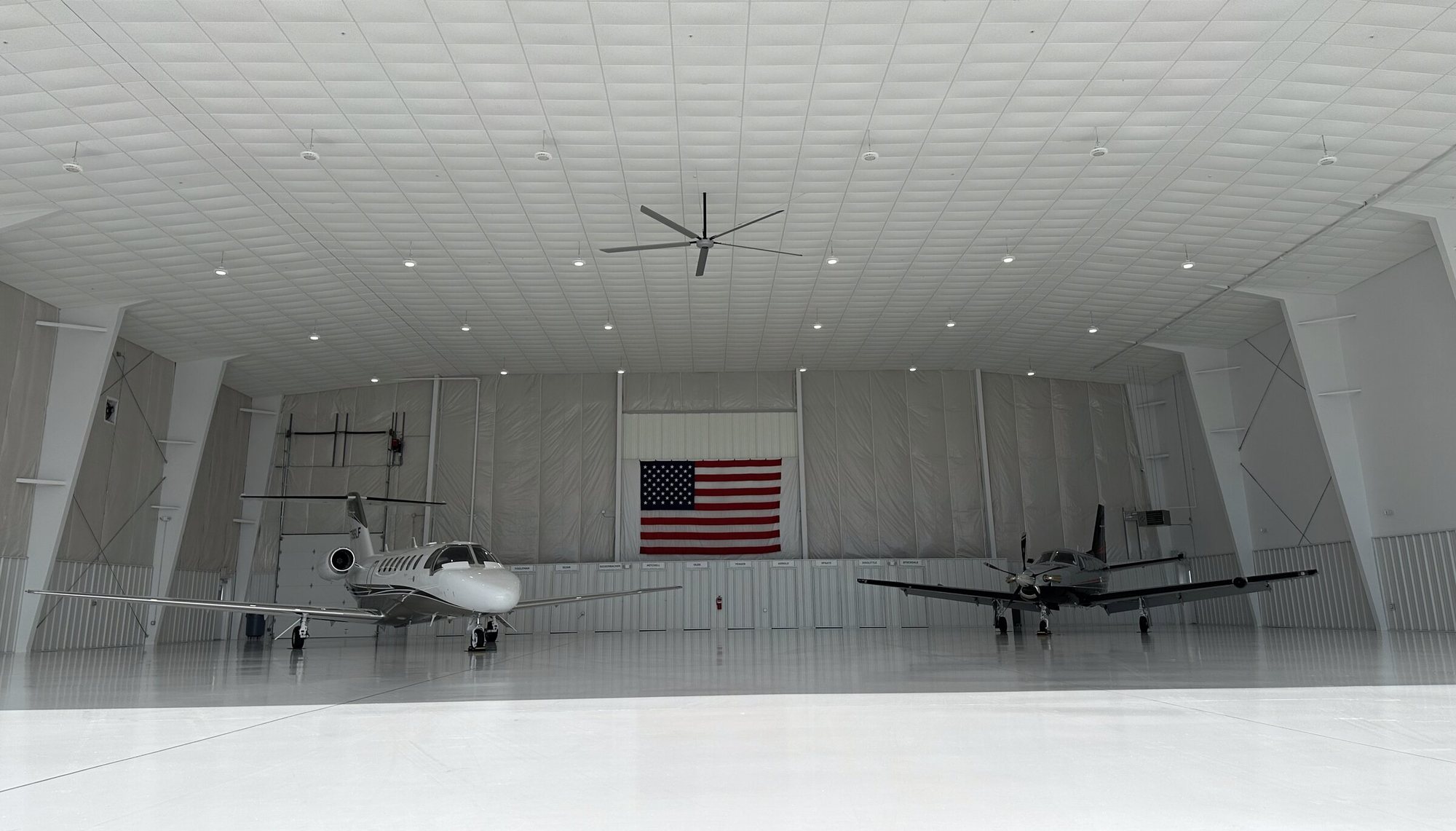 Wide view across the Shelton Aviation hangar floor: a Citation and a turboprop parked on white epoxy under high LED lighting