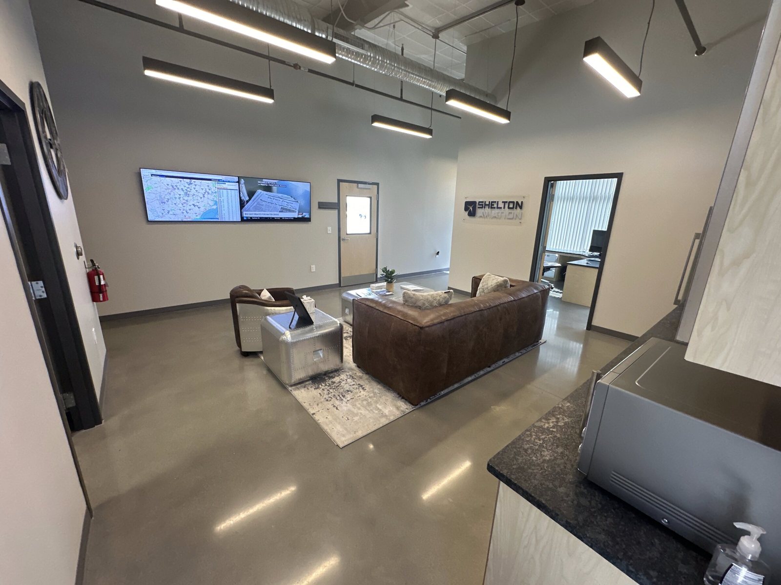The Shelton Aviation lounge: leather seating, a kitchenette counter, and wall screens showing weather and the hangar